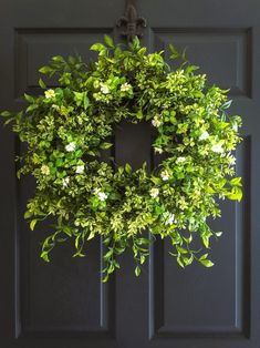 a green wreath hanging on the front door with white flowers and greenery around it