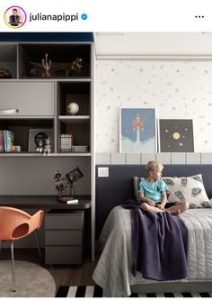 a little boy sitting on top of a bed next to a desk and book shelf