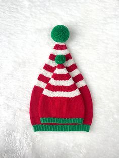 a red and white knitted hat with a green pom - pom