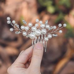 a hand holding a hair comb with pearls and leaves on the top, in front of a blurred background