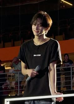 a young man holding a microphone while standing next to a railing in front of an audience