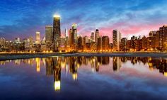 the city skyline is lit up at night with its lights reflecting in the still water