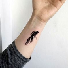 a woman's arm with a small black fish tattoo on the left side of her wrist