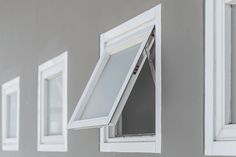 three windows with white trim on the side of a wall and one has a window pane