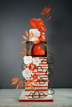 a red and white wedding cake with flowers on the top is surrounded by orange leaves