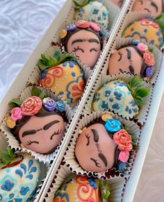 there are many chocolates in the box with faces painted on them and decorated with flowers