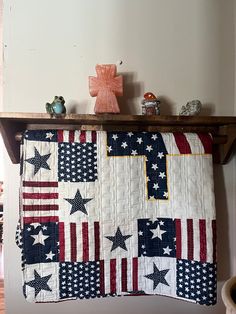 an american flag quilt hanging on a shelf in a room with white walls and wood floors