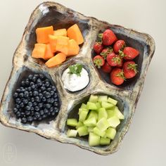 an assortment of fruits and vegetables are arranged in a divided tray on a white surface