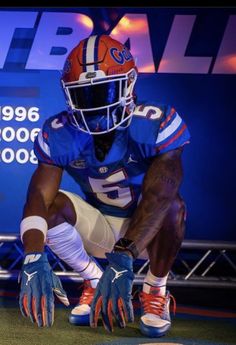 a football player kneeling down on the field with his hands in his pockets and wearing blue gloves