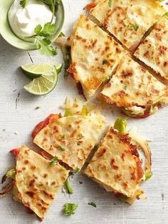 several quesadillas cut into squares on a cutting board with limes and sour cream in the background