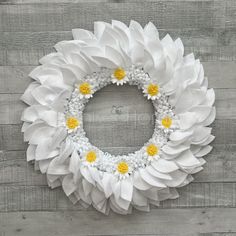 a white wreath with yellow flowers hanging on a wooden wall in the shape of a sunflower