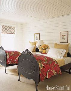 two beds in a room with white walls and carpeted flooring, one has a red blanket on it