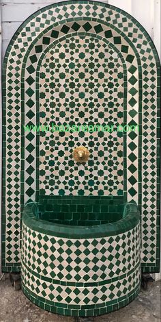 a green and white tiled fountain with a gold faucet