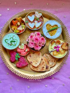 an assortment of food items displayed on a platter with pink table cloth and gold trim