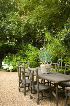 a wooden table and chairs sitting in the middle of a gravel path surrounded by trees