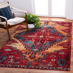 a red rug with an ornate design on the floor next to a chair and potted plant