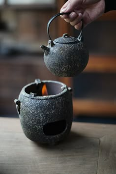 a person is holding a teapot with a flame in it on a wooden table