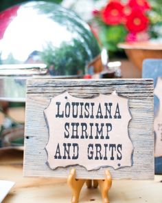 there is a sign that says, louisiana shrimp and grits on the table in front of some potted plants