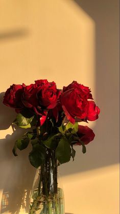 a vase filled with red roses sitting on top of a table next to a wall