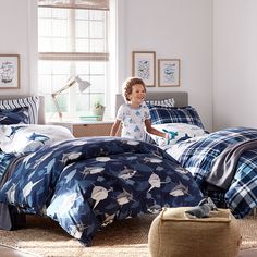 a young boy standing in front of a bed with blue and white comforters