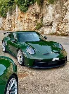 two green sports cars parked next to each other in front of a rocky mountain side