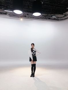 a woman standing in front of a white wall wearing black boots and a sweater over her shoulders