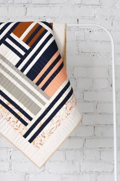 a quilt hanging on a clothes rack in front of a white brick wall with an ironing board underneath it