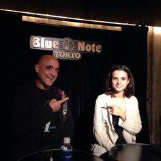 two people standing next to each other in front of a black background with a blue note logo on it