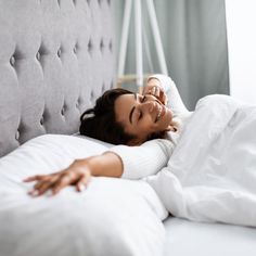 a beautiful woman laying on top of a bed next to a white comforter and pillows