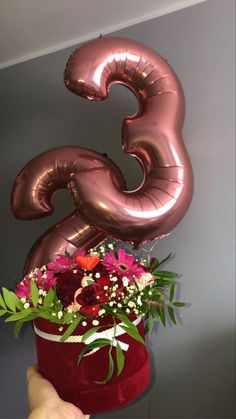 the number two balloon is being held up by a woman's hand with flowers in it