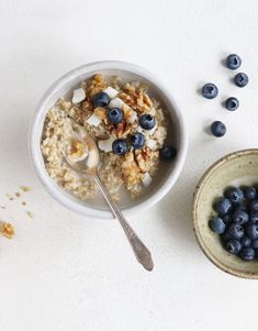 a bowl of oatmeal with blueberries and nuts next to a spoon