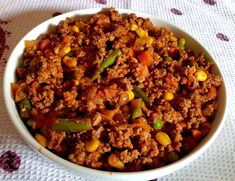 a bowl filled with meat and vegetables on top of a white table cloth next to a spoon