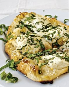 a white plate topped with a pizza covered in cheese and herbs on top of it