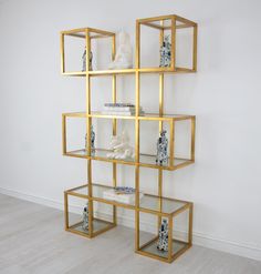 a gold shelving unit with glass shelves and vases on each shelf, against a white wall