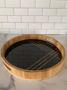 a round wooden tray with black glass in it on a marble countertop next to a white brick wall