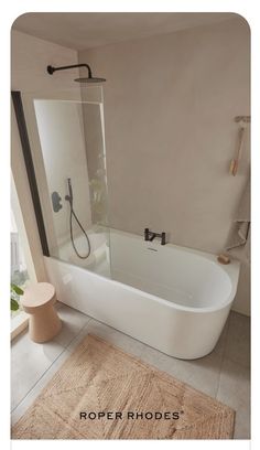 a white bath tub sitting next to a window in a bathroom with a rug on the floor