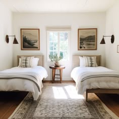 two beds in a room with white walls and wooden floors, one has a rug on the floor