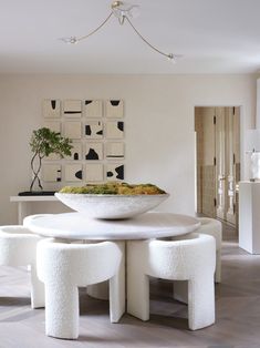 a white table topped with a bowl filled with food next to two stools and a potted plant