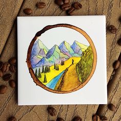 coffee beans are scattered around a card with a drawing of a mountain scene in the middle