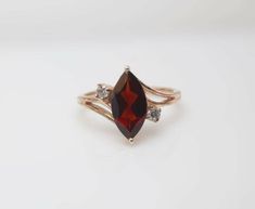 a close up of a ring with a red stone and two white diamonds on it