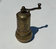 an old fashioned brass pepper mill on a white surface with a shadow from the top