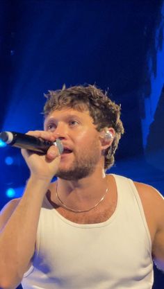 a male in a white tank top is holding a microphone and looking up at the sky