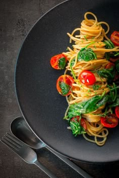 pasta with tomatoes and spinach on a black plate