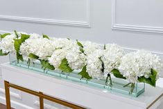 white flowers are arranged in glass vases on a table next to a gold framed wall