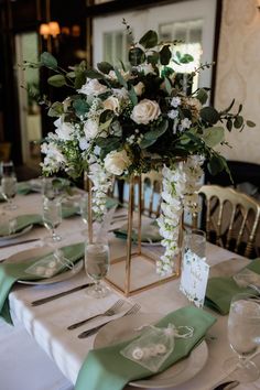 the table is set with white and green flowers in vases, napkins, and place settings