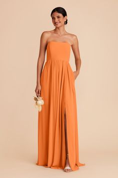 a woman wearing an orange strapless dress and holding a flower in her right hand