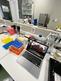 an open laptop computer sitting on top of a white counter next to plastic containers filled with liquid