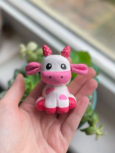 a small toy cow sitting on top of a hand next to a potted plant