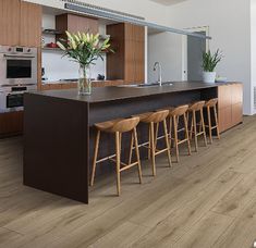 a kitchen with wood flooring and counter tops, along with bar stools in front of an island