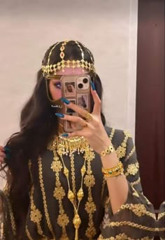 a woman is taking a selfie with her cell phone while wearing an elaborate gold and black outfit